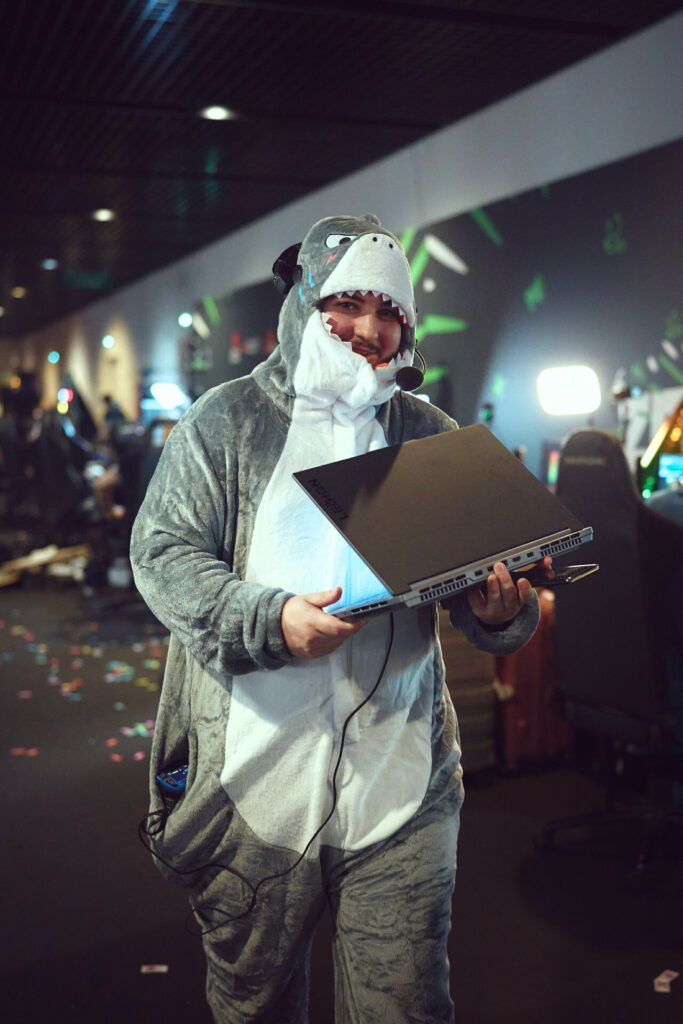 Deployer in a shark onesie carrying a laptop through the ZEVENT 2026 production floor