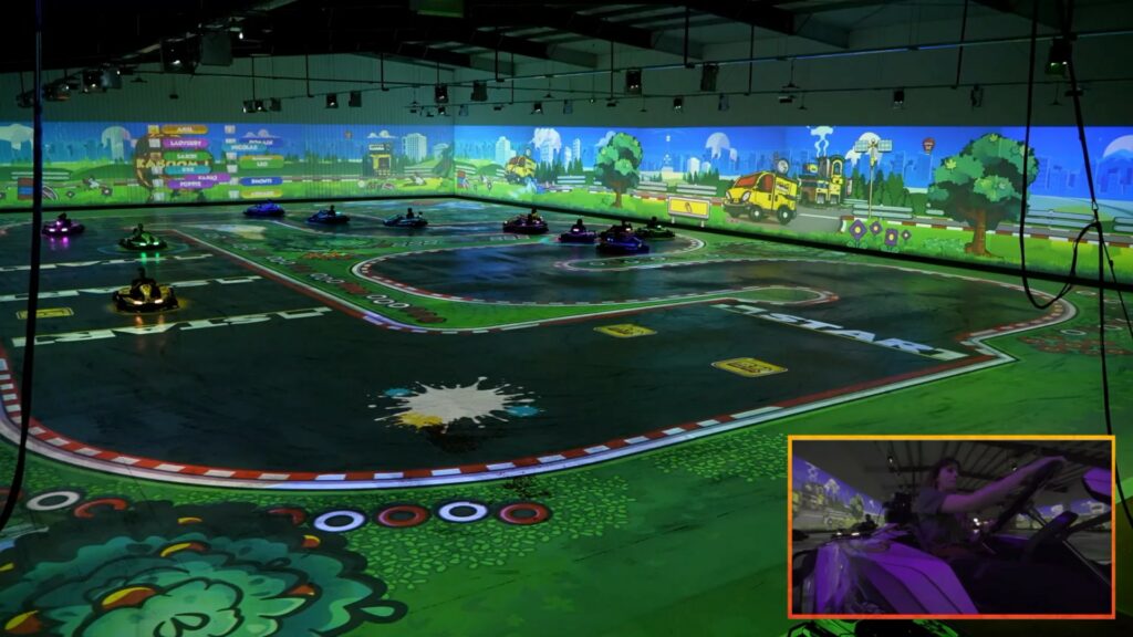 Wide shot of the BattleKart Dijon arena with the game track projected on the floor and an onboard camera inset